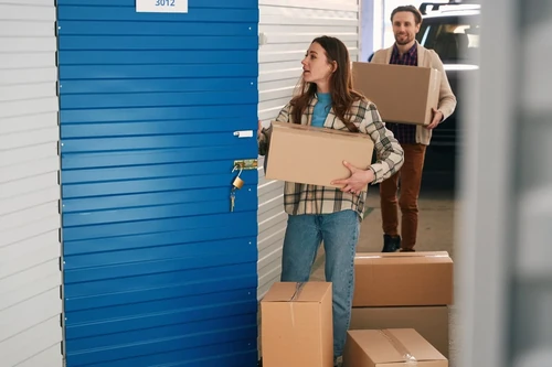 A woman carrying a box while opening a storage unit.
