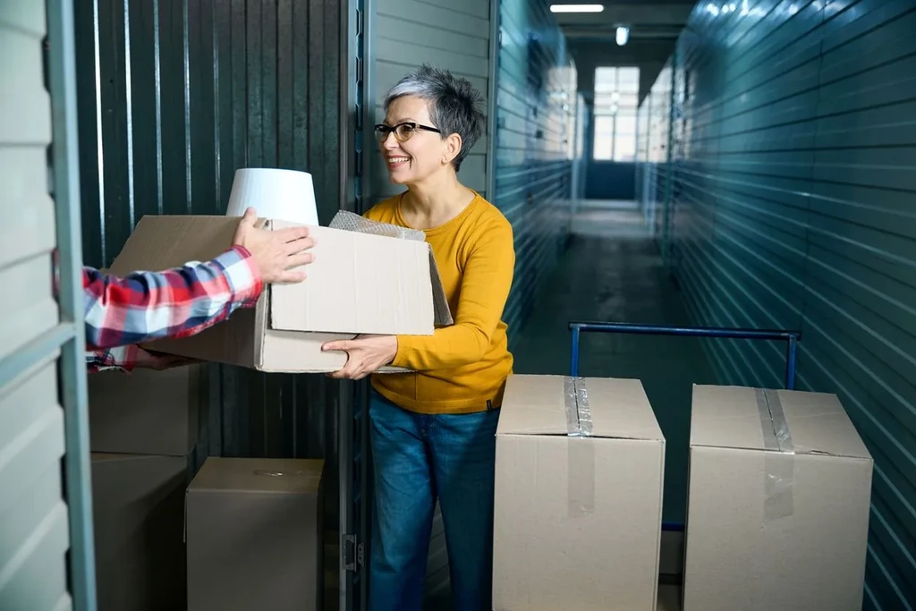 An older woman handing a brown storage box to a man in a storage unit.